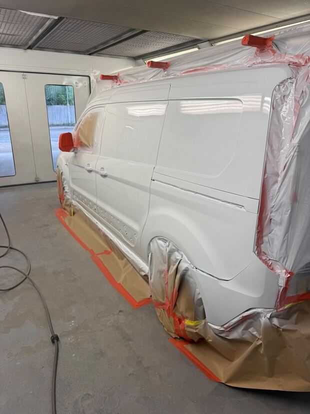 The same white van masked along the side, painted, in the spray booth